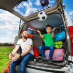 pappa och son leker med en fotboll när de sitter i bagageutrymmet av sin bil